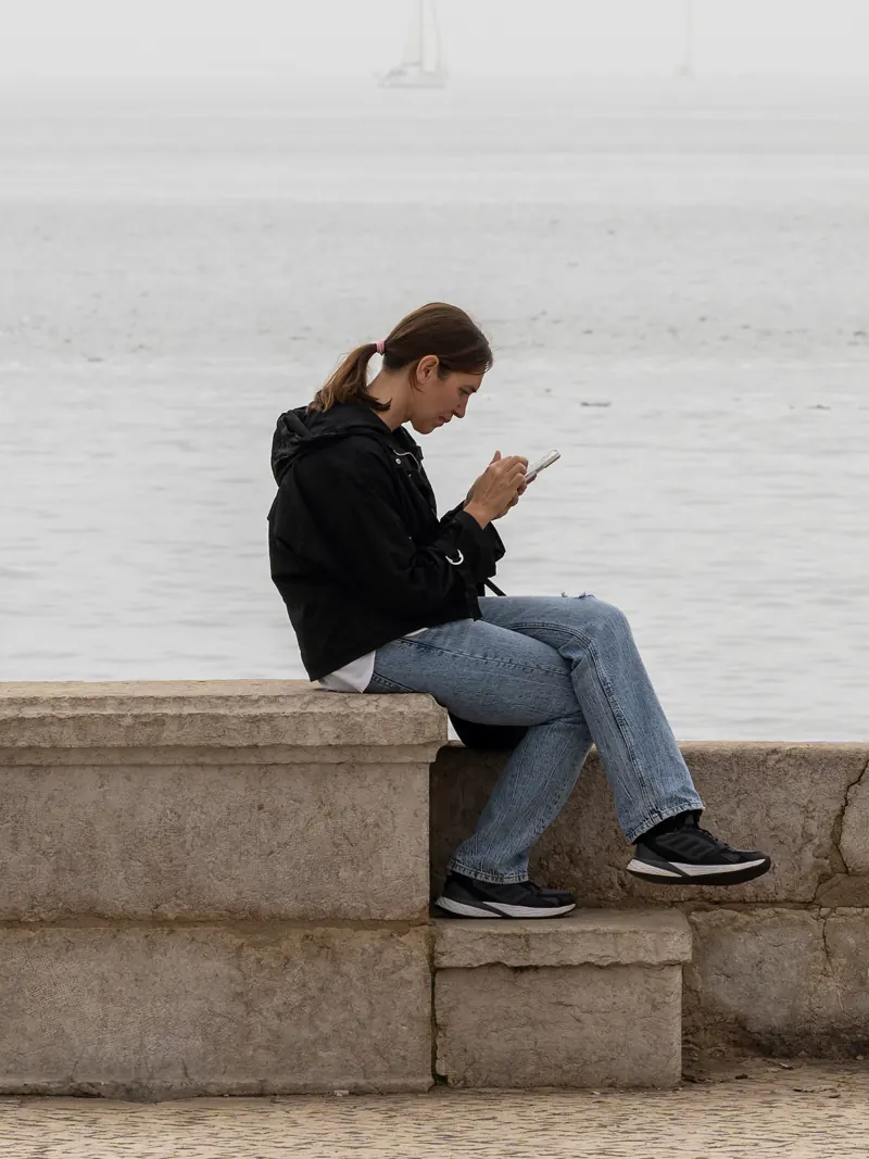 A woman checking her phone on a seafront wall in Lisbon